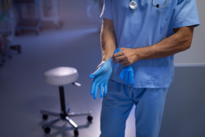 Mid section of a surgeon putting on rubber gloves at the hospital
